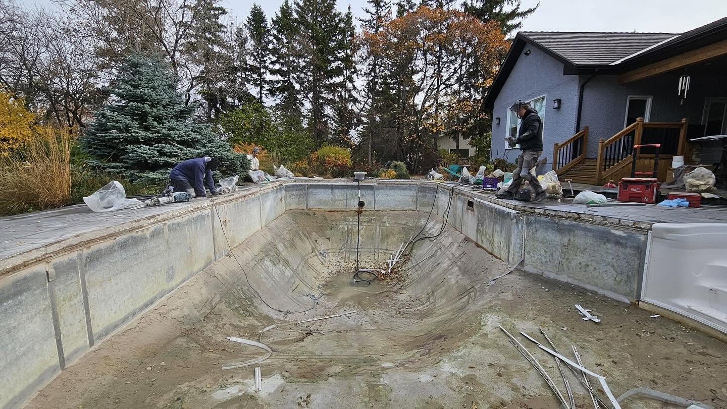 Workers renovating a drained backyard pool with the liner removed