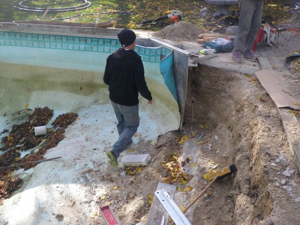 Worker beside an exposed pool wall and excavated deck during an inground pool repair